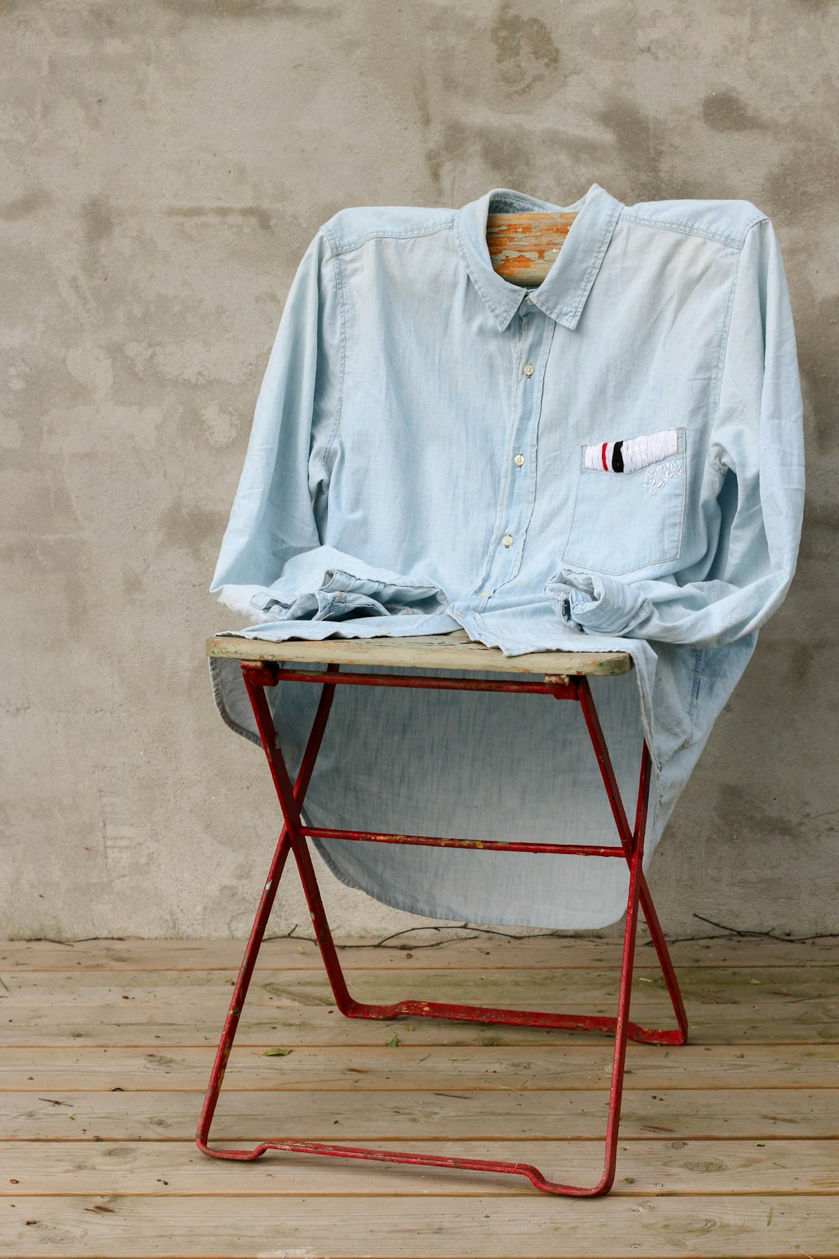 A chambray shirt laid over a red folding stand on a concrete floor